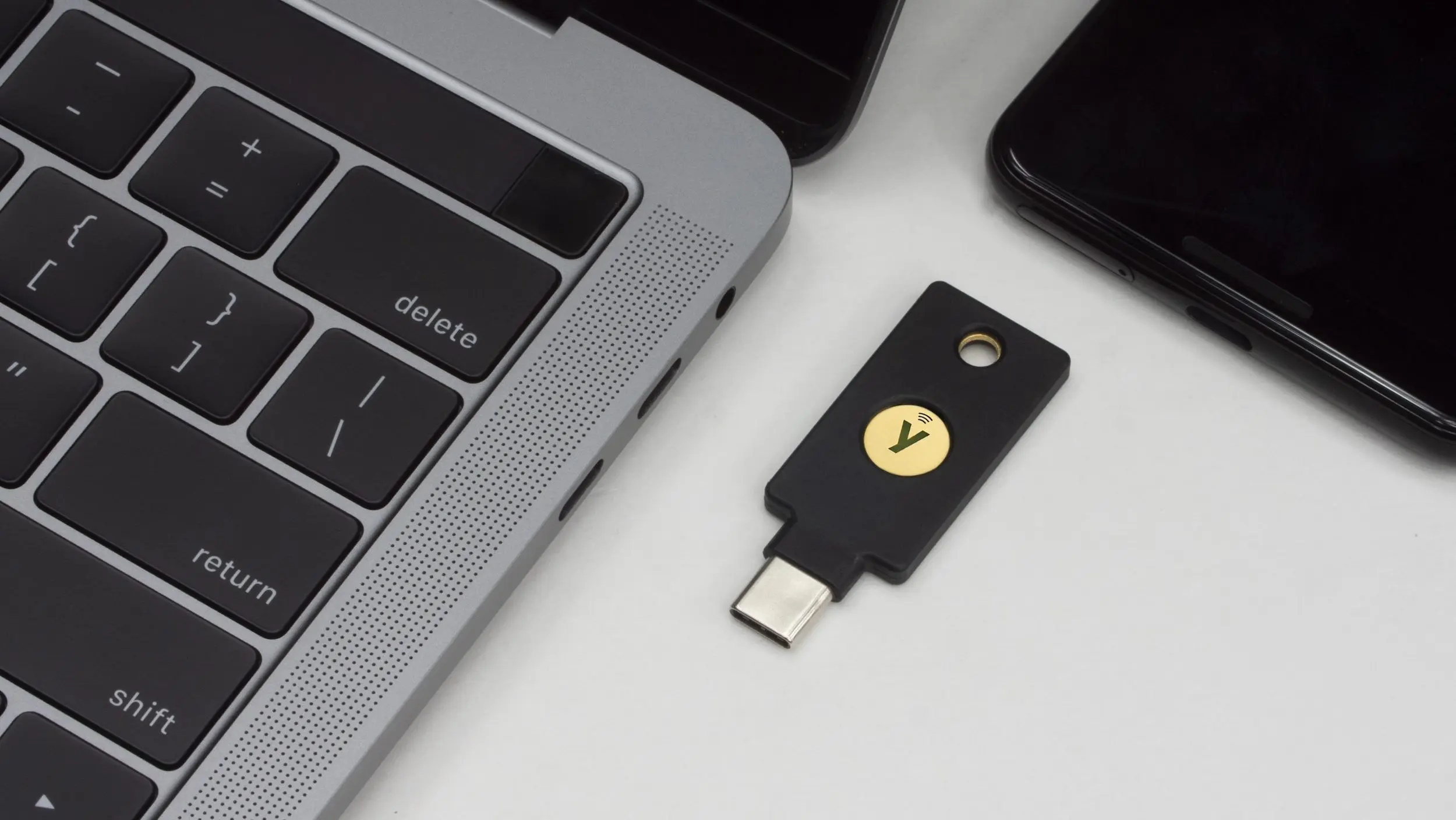 Photo of YubiKey on a table between a MacBook and a phone.